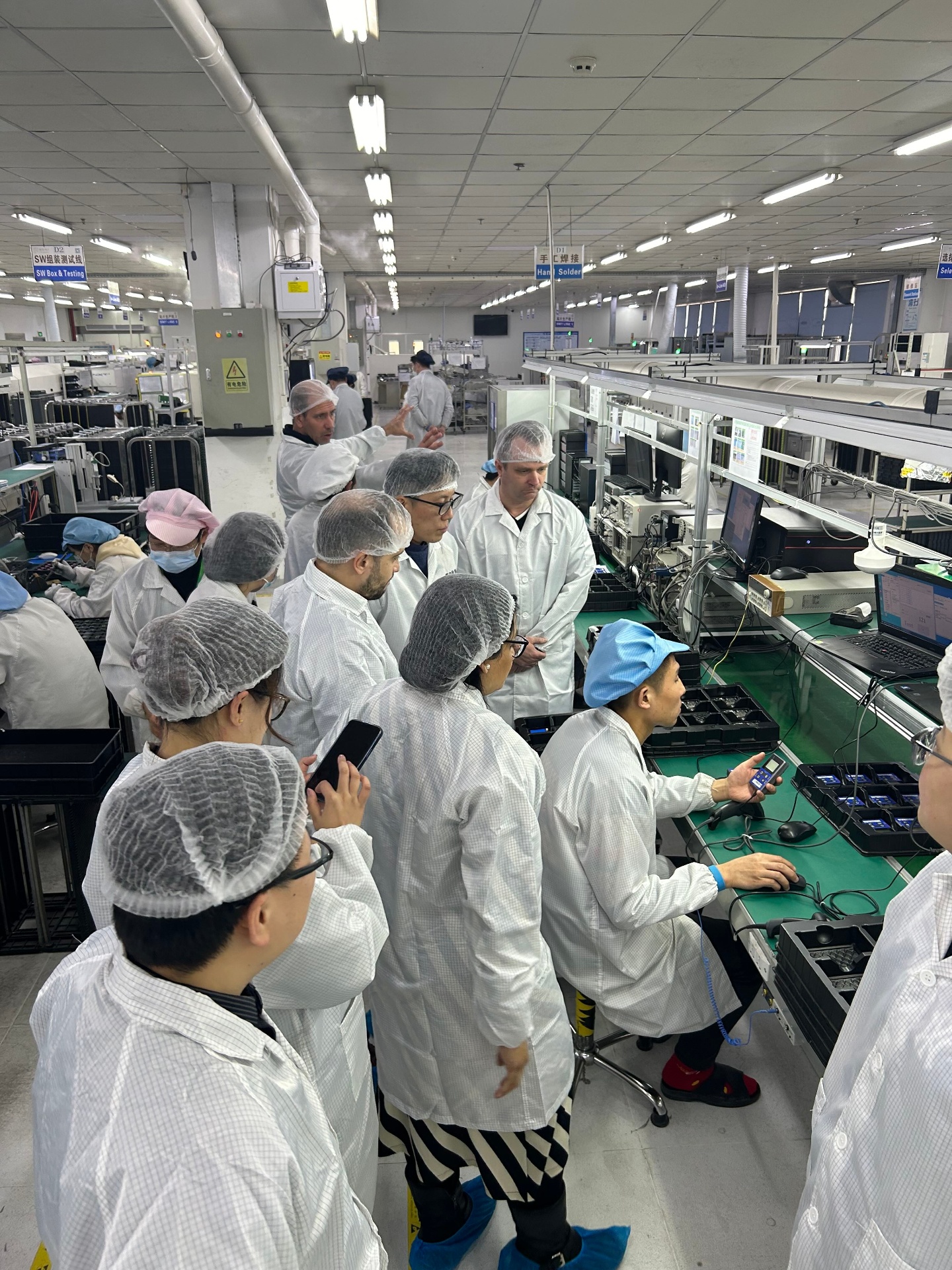 Audit team in ESD coats observing final test and calibration of tracking devices on a production line